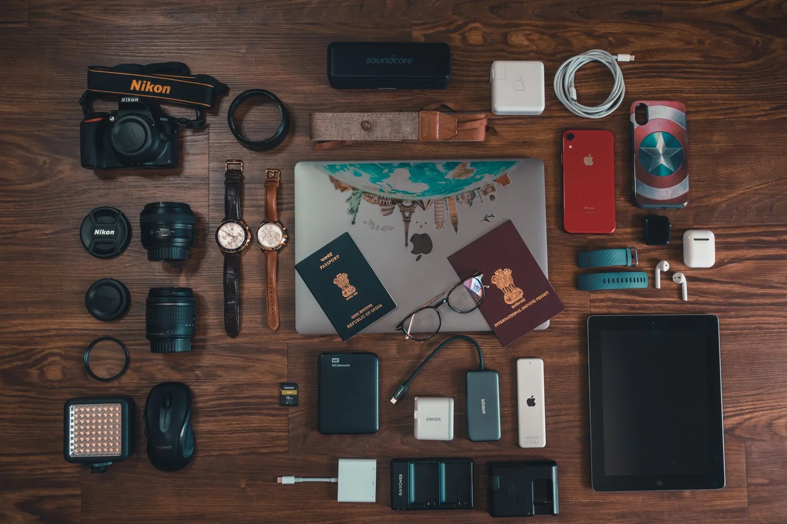 Flat lay of passports, camera gear, chargers, cables and personal electronics on a wooden table