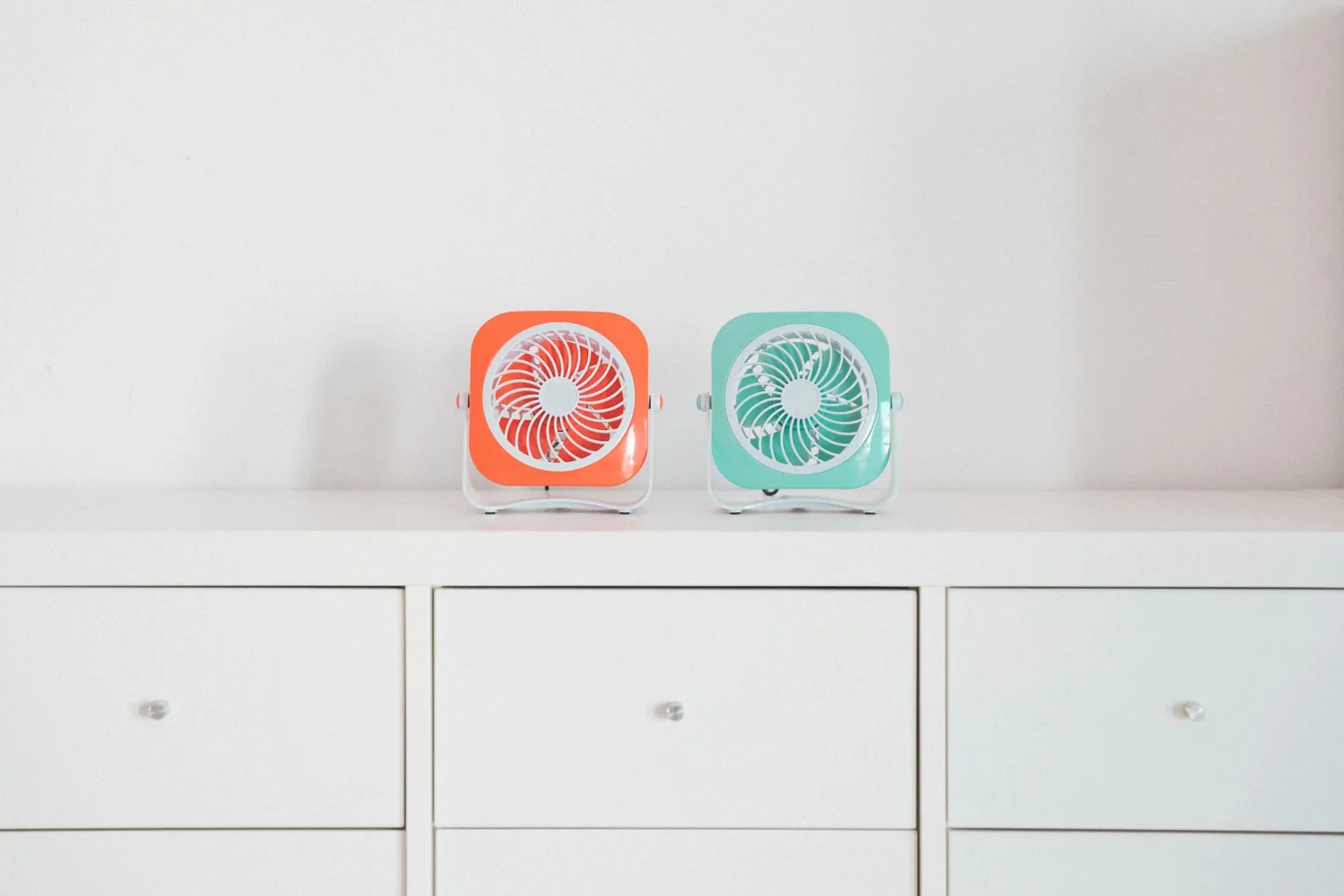 Two compact red and green portable desk fans on a white cabinet