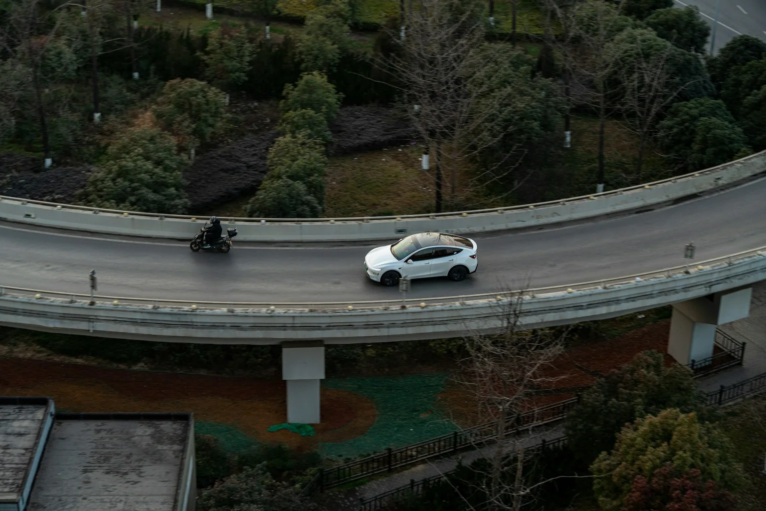 White Tesla Model Y driving on an elevated road bordered by trees